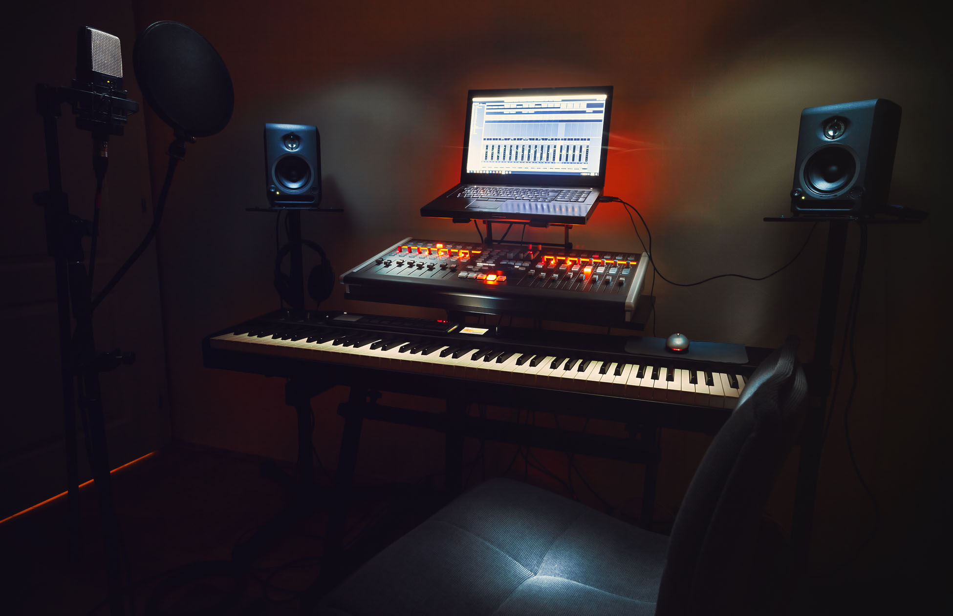 Interior of a small bedroom recording studio, details of equipment, microphone in foreground and modern mixing console with laptop in background.